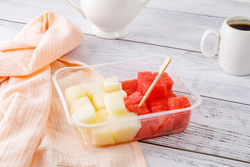 Fruit salad with watermelon and melon in a plastic container on a wooden background.