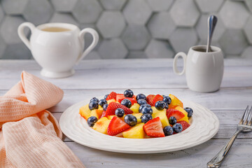 Fruit salad with pineapple, strawberries and blueberries on a white plate.