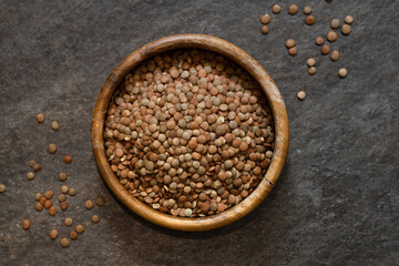 raw lentils in a wooden bowl, legumes scattered on the table