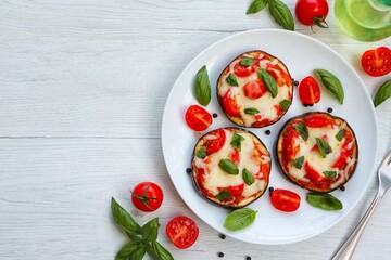 Mini eggplant pizzas-eggplants with pizza sauce,olive oil,mozzarella cheeses,tomatoes,basil,salt and peppers on plate with white wood background.Healthy summer vegetarian food.Top view.Copy space