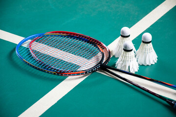 Badminton rackets and white cream badminton shuttlecocks after playing or after games on green floor in indoor badminton court, soft focus, concept for badminton lovers around the world.