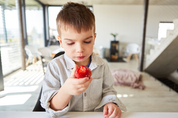 Kleiner Junge hält eine frische Erdbeere in seiner Hand