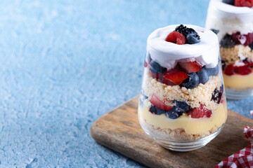 Trifle dessert with berries and cream on blue background. Copy space