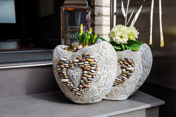 Spring flowers in heart-shaped stone pots stand on a staircase at the entrance to the house