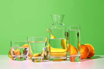 Still life with fresh fruits kiwi, banana, orange and glasses with water on table over green background. Bright colors. Smoothie ingredients