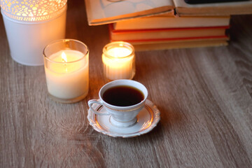 Cup of tea or coffee, plate of cookies, books, e-reader, pencil and lit candles on the table. Selective focus.