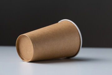 Disposable cardboard biodegradable glass on a white table, gray background.