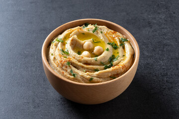 Chickpea hummus in a wooden bowl garnished with parsley, paprika and olive oil on black slate...