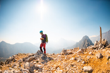 girl climber in a helmet and with a backpack stands on a mountain range against the backdrop of...