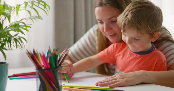 Mother and child drawing with pencils sitting at the desk at home. Happy family