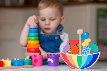 Fototapeta na wymiar Balancing toys. A little boy is playing educational games. Children's wooden toy in the form of an umbrella, a colored pyramid and logic toys for children. Montessori Games for child development.