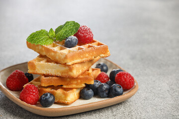 Waffles with berries in plate on grey table