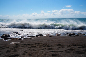 Impresionante orilla de la playa de arena negra de Ajuy con el mar turquesa agitado con sus olas rompiendo y formando una espuma blanca durante la puesta de sol con la luz del sol en Fuerteventura