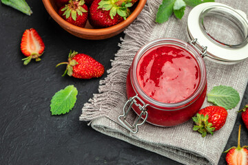 Strawberry jam in the glass jar with a spoon at dark table. top view