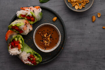 Summer rolls with fresh vegetables and shrimps or prawns and peanut and chili sauce on dark grey background. Vietnamese appetizer. Top view. Healthy food concept