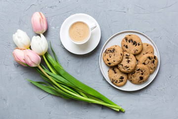 Cup of coffee mug with coffee, cookies and tulips on a colored background. Greeting spring card top view