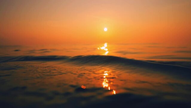 Slow Motion ocean surface from underwater at sunset with rays of light. Crystal clear breaking ocean wave with waving waterline. Sunrise over calm sea. Dawn over horizon, ocean, water - timelapse or