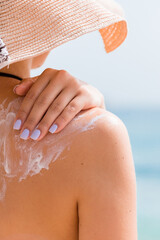 Sunscreen sunblock. Woman in a hat putting solar cream on shoulder outdoors under sunshine on...