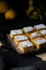 Lemon bars decorated with icing sugar on a black background. Freshly homemade Lemon squares.