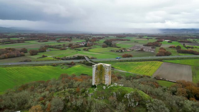 High angle aerial orbit of sandiás tower, ourense, spain, above farmland on stormy day