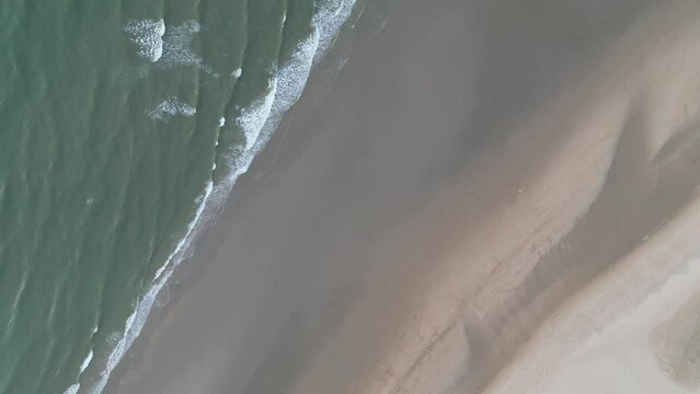 Spinning drone footage of sea waves crashing into sandy beach in Dunkerque (Dunkirk), France