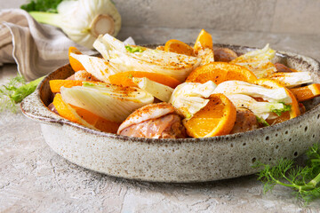 chicken legs with fennel and orange on a round baking sheet on the table