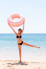 Naklejka na ściany i meble Happy woman on the beach playing with an inflatable donut ring. Summer holidays and vacation concept