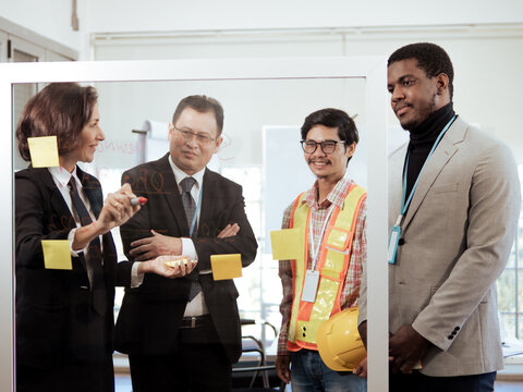 Group of diverse ethnic construction engineer architect meeting brainstorming project plan by writing on glass board. Asian man, multiracial partner and caucasian manager discussion, diversity team
