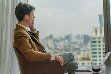 Back side view of a handsome young white businessman talking on the phone and looking out the window view of city skyline in a business district area - obrazy, fototapety, plakaty