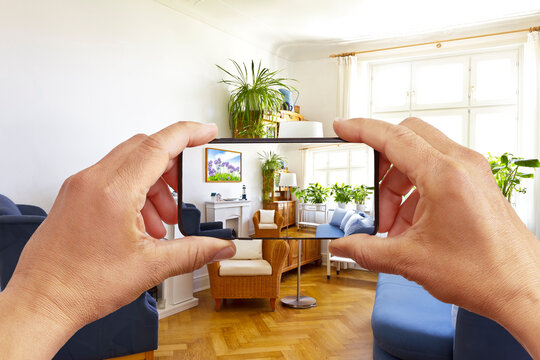 Augmented reality concept: hands holding smart phone with AR interior decoration app, visualising the living room with additional photo frame.