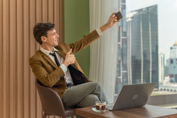 Handsome young white businessman selfie on the phone and in front the window view of city skyline in a business district area