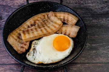 fried egg, bacon and fried vegetables in skillet with spoon