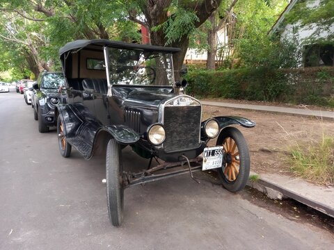 Vintage car black 1920s Ford Model T double phaeton parked in the street. Trees in the background.