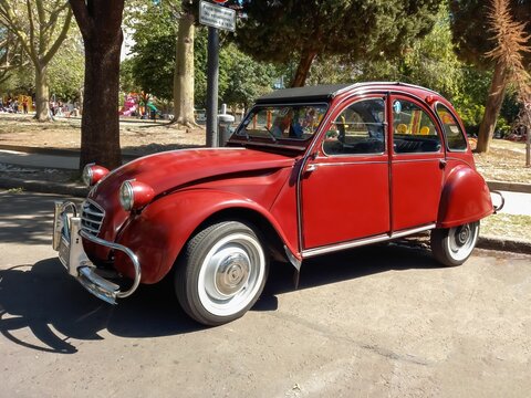old red burgundy popular Citroen 3CV 1960-1979 in the street in front of a park. Classic car show.