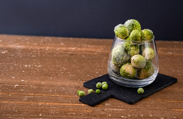 Frozen, fresh Brussels sprouts. Brussels sprouts in a clear glass jar. Texture of frozen Brussels sprouts. Brussels sprouts on a dark background. Horizontal photo. copyspace