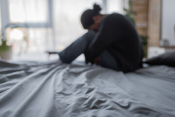 Blurred multiracial woman with depression sitting on bed at home.