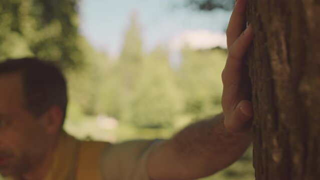 Mid adult Caucasian male scouter putting his hand on trunk while examining tree bark in summer forest