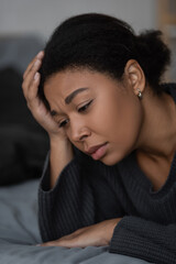 Portrait of upset multiracial woman lying on blurred bed at home.