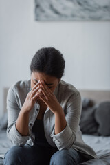 Depressed multiracial woman crying on blurred bed at home.