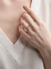 Close-up shot of a gold ring decorated with sparkling crystals on a female hand. Open ring is on the finger of a lady wearing a white blouse. Woman jewelry concept.