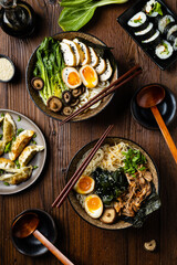 Traditional ramen with jerked pork or chicken.  With udon or ramen noodles. Served in classic bowls. Gyoza dumplings and mushrooms in the background.