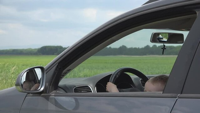 Little kid on front seat of a car waving hand bye-bye