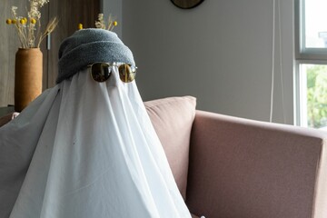 Obraz premium Person wearing a hat and black-rimmed sunglasses over a white cloth resembling a ghost