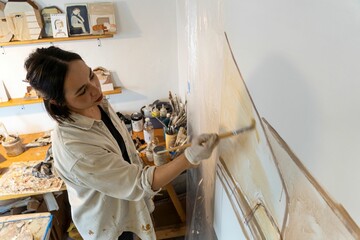Female artist wearing protective painting gloves is focused on creating her masterpiece on a canvas