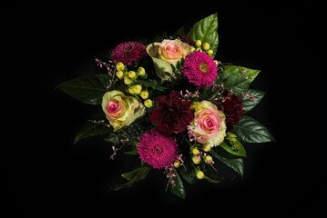 Bouquet of roses, asters and petunias decorated with leaves isolated on a black background