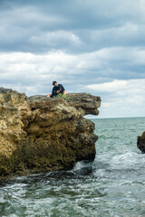 joven rostro no reconocible a la lejania con su perrita disfrutando de un dia nublado junto a la mar 