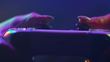 Woman gamer playing online video game on console. Wireless controller close-up under neon color light. Girl presses buttons, using joypad. Hobby, e-sport, macro view