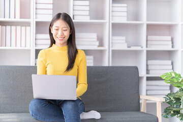 Young Asian woman sitting on sofa holding Teacup and notebook and check email, in the leaving room.