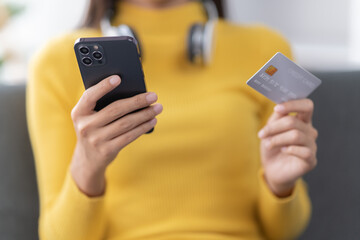 Portrait of asian girl shopping online sitting on sofa, paying bills with credit card, laptop and smartphone, enter card number in mobile phone app to purchase sth in internet store