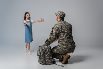 happy kid welcoming father in army uniform during homecoming on grey background.